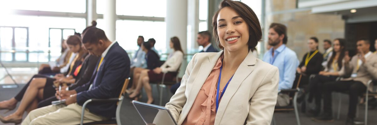 Happy young businesswoman with digital tablet looking at camera during seminar
